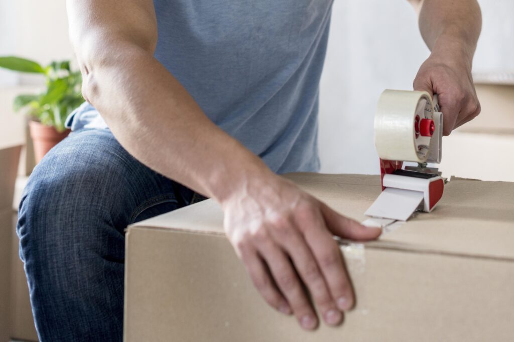 A cropped image of an office mover sealing a moving-out box with packing tape